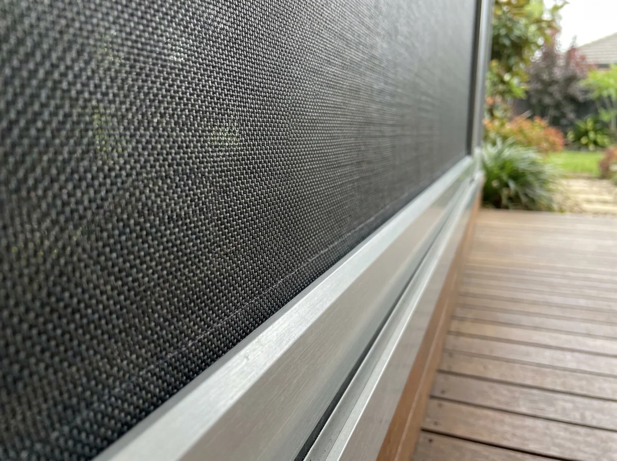 Close-up of a zip screen's woven mesh and aluminium track on a Big Bay timber deck